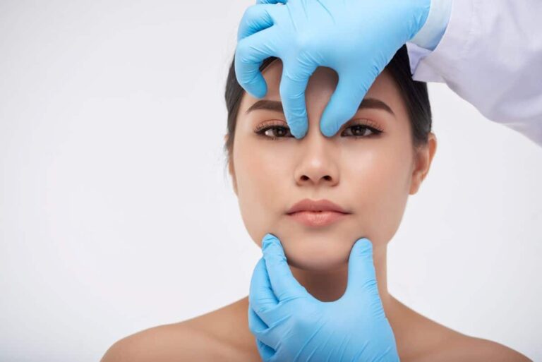 Deviated Septum Diagnosis gloved hands of an ENT gently pinch the bridge of the nose of a female patient who is looking directly at the viewer of the image
